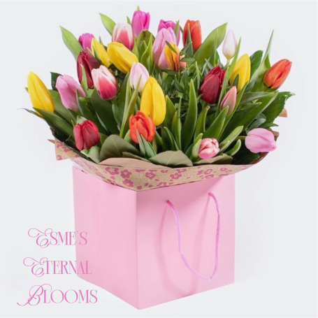 A bouquet of colourful tulips in a pink gift bag with decorative edges.