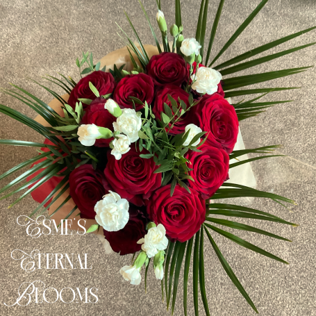 A heart-shaped bouquet of red roses and white flowers with green foliage.