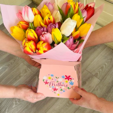 A bouquet of vibrant tulips in shades of pink, yellow, and white with a gift box.